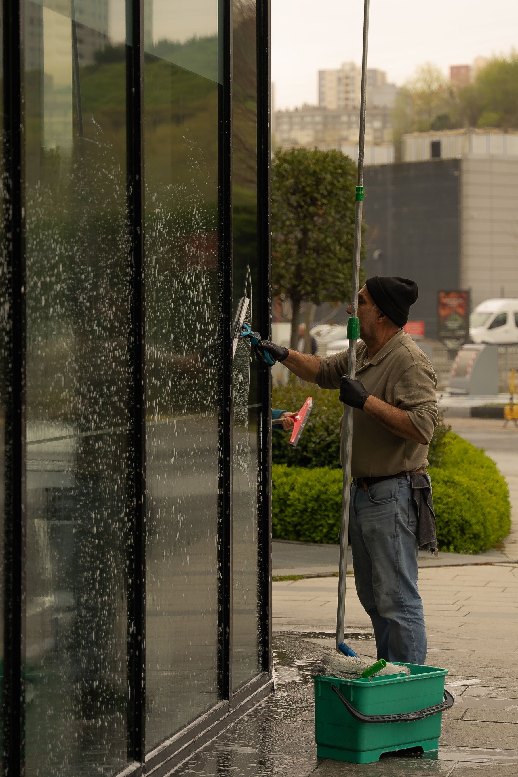Vinduespudser arbejder på en glasfacade med skraber og teleskopstang